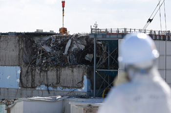 A member of the media, wearing a protective suit and a mask, looks at the No. 3 reactor building at the Fukushima No. 1 nuclear power plant on Feb. 10, 2016. | POOL / BLOOMBERG 
                          